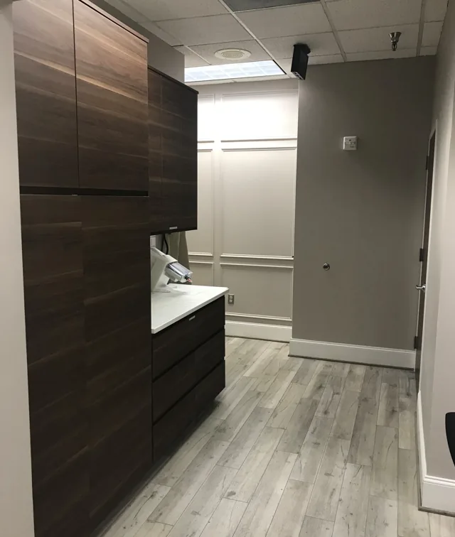 Office interior with dark cabinetry, a sink, window and gray wood-look floor