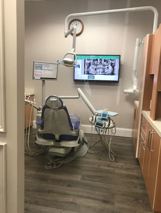 Dental treatment room with a patient chair, overhead light and wall-mounted screen