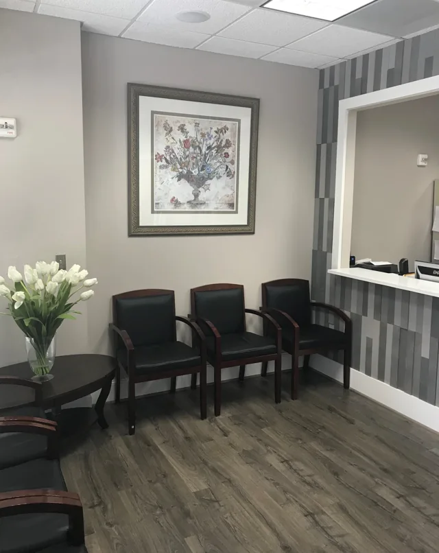 Waiting area with black chairs, flowers, framed artwork and the reception window